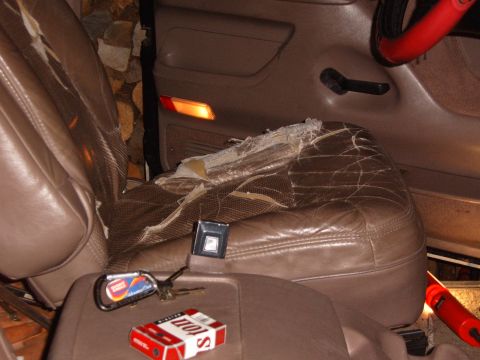 1993 Ford Bronco - Worn tan leather front seats in a truck cab with the seat-bottom upholstery split open to expose foam and burlap backing, plus a seat belt…