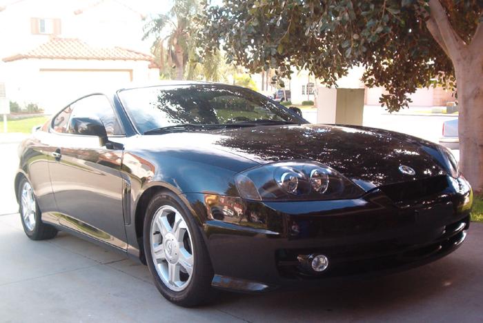 Black Hyundai Tiburon coupe, 3/4 front view, parked in driveway