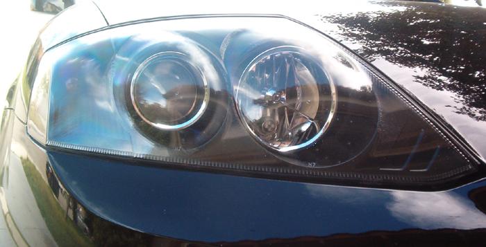 Close-up of dual round projector headlight on a black car with reflections on the lens