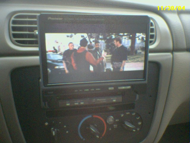 Pioneer flip-out screen head unit playing video in a car's gray center dash, above rotary HVAC knobs