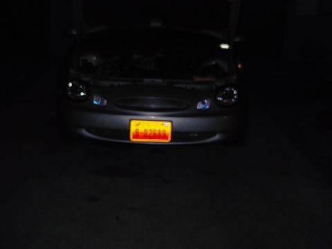 1999 Ford Taurus - The front of a 1999 Ford Taurus is visible at night, with the hood up and headlights on.