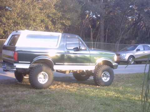 1992 Ford Bronco - Side view of a lifted green 1992 Ford Bronco with a white removable top.