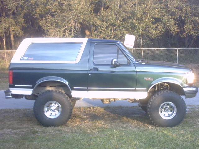 Lifted dark green Ford Bronco with white top and big all-terrain tires, side view on grass