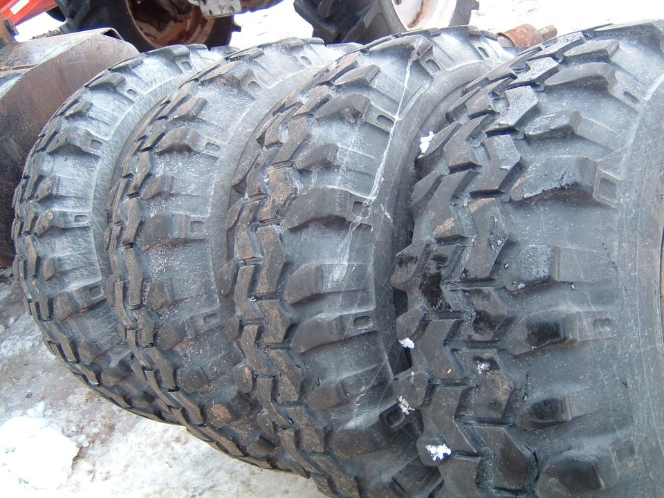 Four mud-terrain tires lined up leaning together on snowy ground