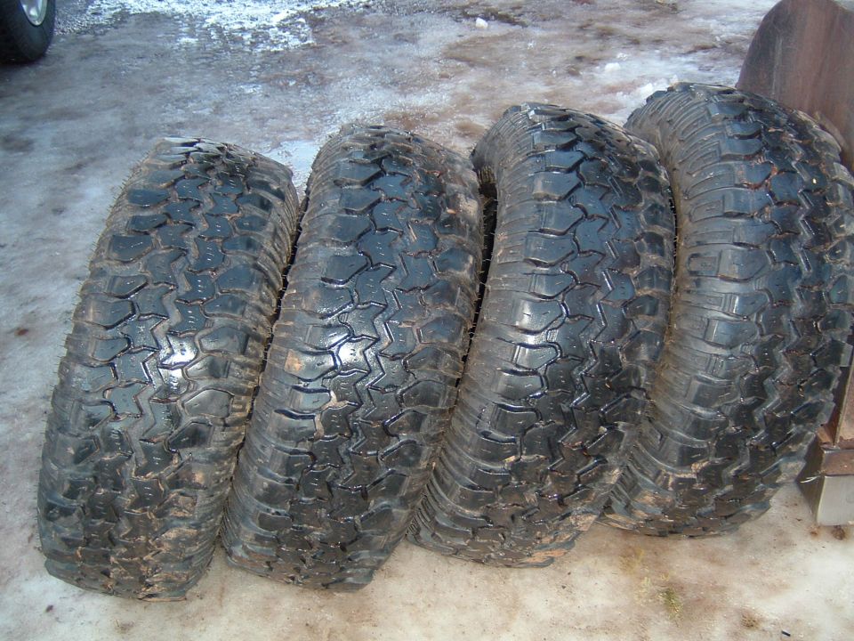 Four used mud-terrain tires lined up on a concrete garage floor