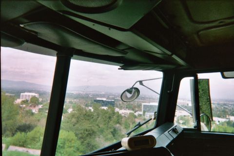 1990 Ford Bronco - interior of a high cab looks out through the windshield over a green hillside toward valley buildings and distant hills.