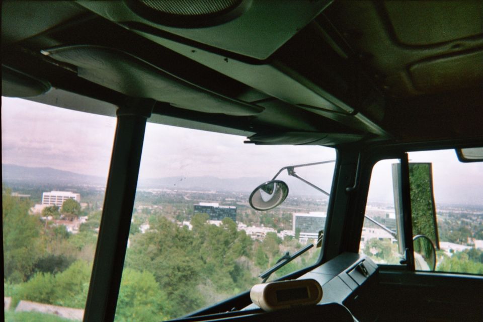 View from inside a truck or bus cab through the windshield over a green valley with buildings and hills