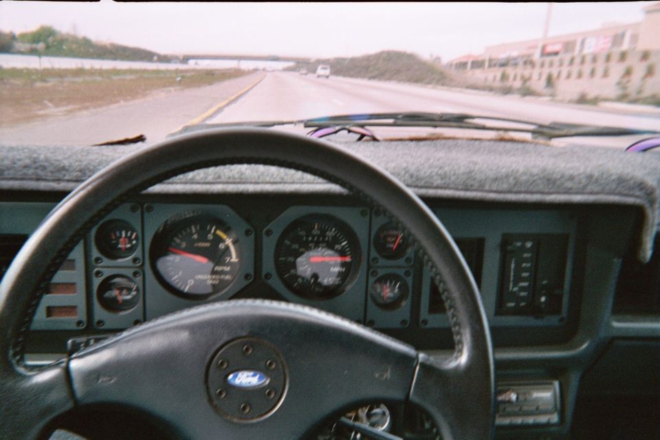 Driver's view of a Fox-body Mustang Ford steering wheel and gauges on an open highway