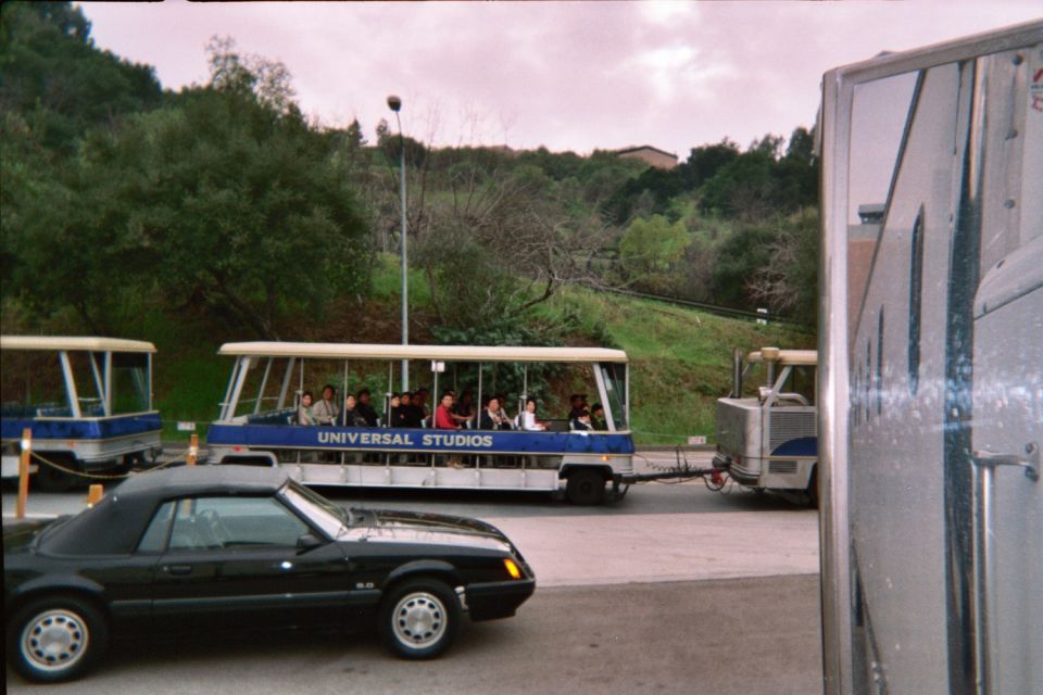 Black 1985 Ford Mustang convertible parked next to a Universal Studios tram tour vehicle