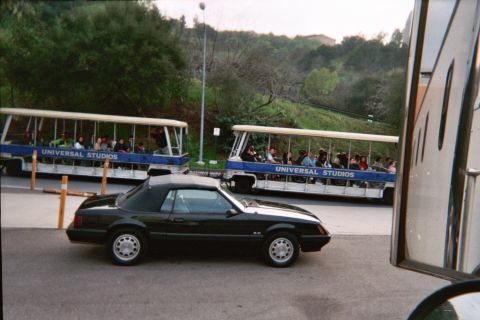 1985 Ford Mustang - A black convertible is parked near Universal Studios trams.