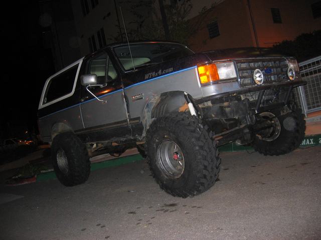 Lifted gray two-door SUV with large mud tires at night, front 3/4 view