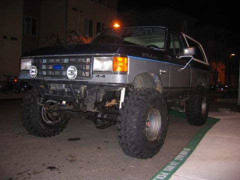 1989 Ford Bronco - This modified Ford Bronco features oversized tires and a prominent 4x4 decal on the front grille.