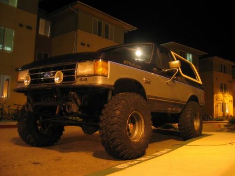 1989 Ford Bronco - This modified 1989 Ford Bronco features oversized tires and a prominent front bumper, seen at night.