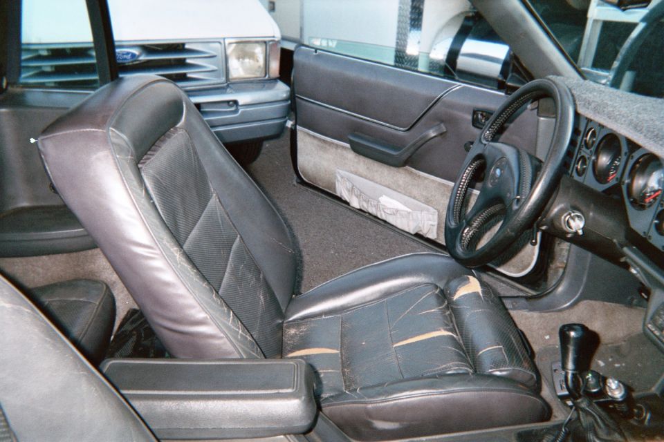 Fox-body Ford Mustang interior with gray bucket seats, manual shifter and gauge pod