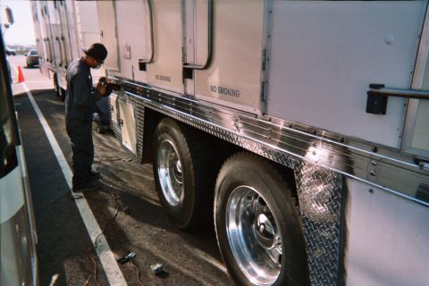 1990 Ford Bronco - worker kneels at the side of a large white trailer with polished aluminum wheels and "No Smoking" labels in a paved lot.