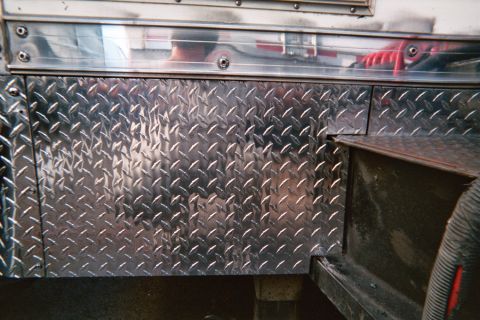 1990 Ford Bronco - Close-up of polished aluminum diamond-plate storage doors and compartments mounted along the lower side of a vehicle.