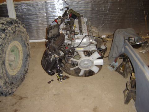 1992 Ford Bronco - Engine assembly with fan and air intake, resting on a tire, with a muddy tire visible to the left.