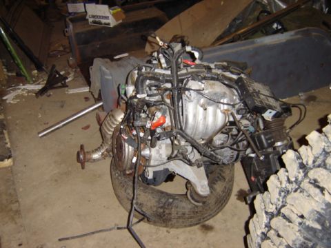 1992 Ford Bronco - Engine assembly, likely removed from a vehicle, rests on a tire in a cluttered garage setting.