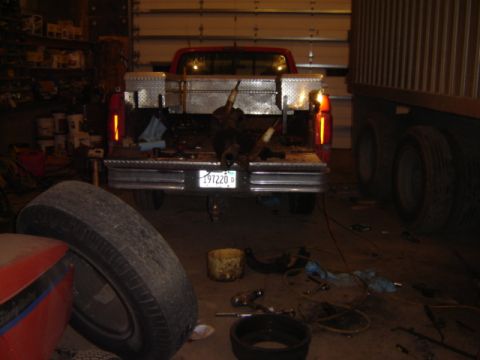 1992 Ford Bronco - Rear view of a red pickup truck with a toolbox and animal carcass in the bed, parked next to a large trailer.