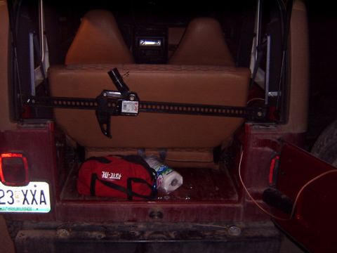 1998 Jeep TJ - The rear cargo area of a red Jeep contains a Hi-Lift jack, a red tool bag, and paper towels.