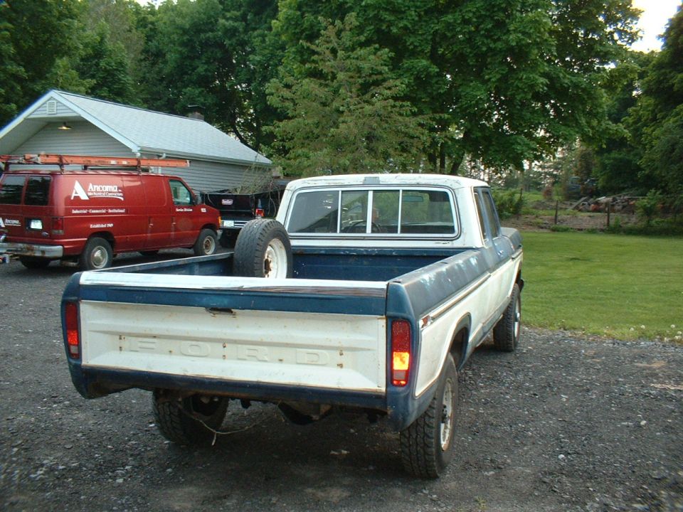 1978 Ford F-250 pickup truck, rear view, with a spare tire in the bed. A red van is parked to the left