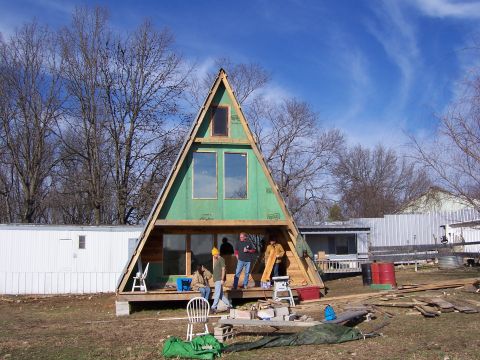 1999 Jeep TJ - Construction progresses on an A-frame house, with workers present on the porch and a mobile home visible in the background.