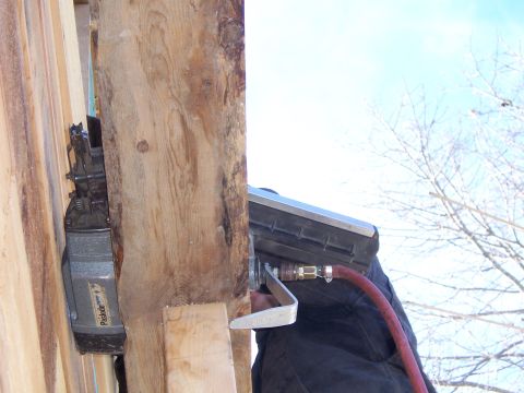 1999 Jeep TJ - A nail gun is being used to attach wood to a larger beam, with a blue sky and bare tree branches visible in the background.