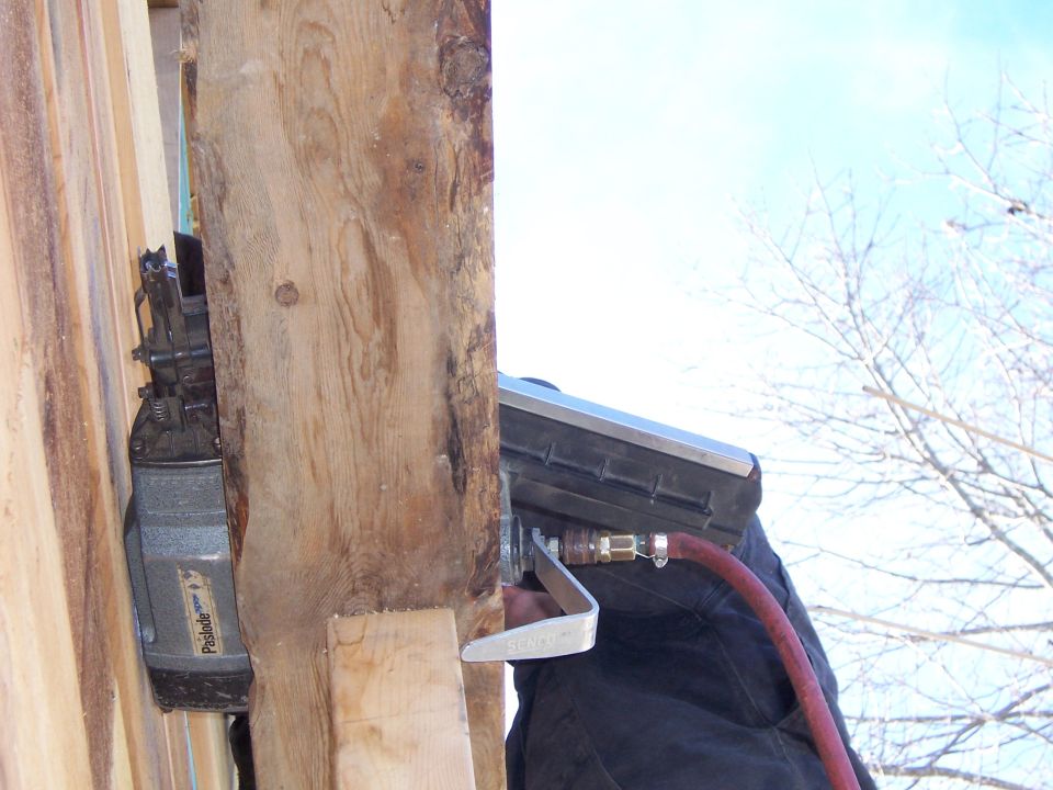 Nail gun with red hose attached to a wooden beam