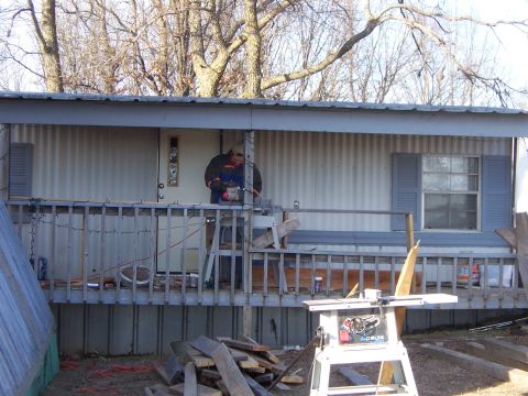 1999 Jeep TJ - A man uses a chainsaw to work on a porch, with a table saw visible in the foreground.