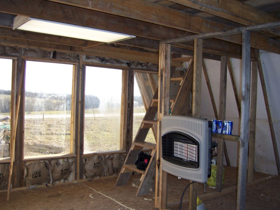 Interior of an unfinished wood-framed cabin with windows and a propane heater