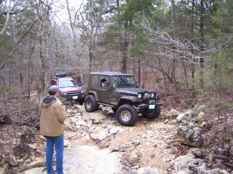1999 Jeep TJ - Two 4x4 vehicles tackle a challenging rocky path in a wooded area during an off-road excursion.