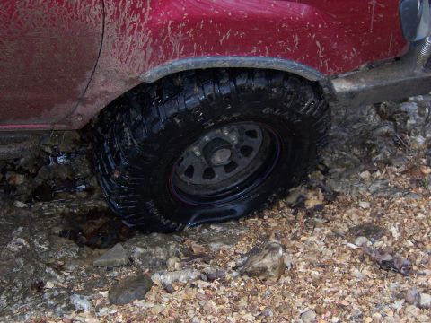 1999 Jeep TJ - Flat tire on a red 1999 Jeep TJ during an off-road excursion.