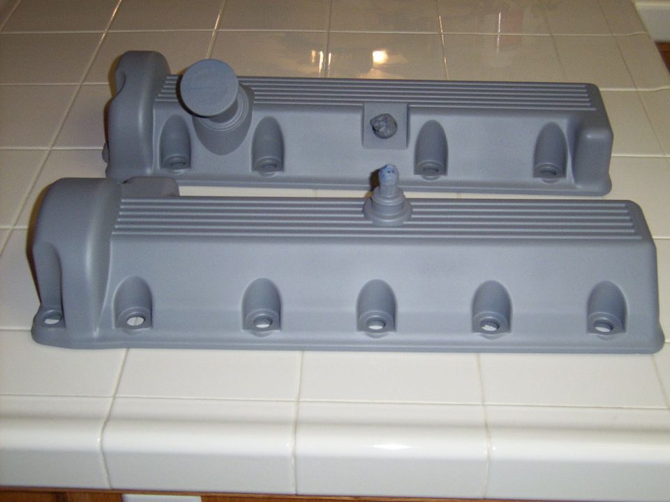 Two gray engine valve covers sit on a tiled surface