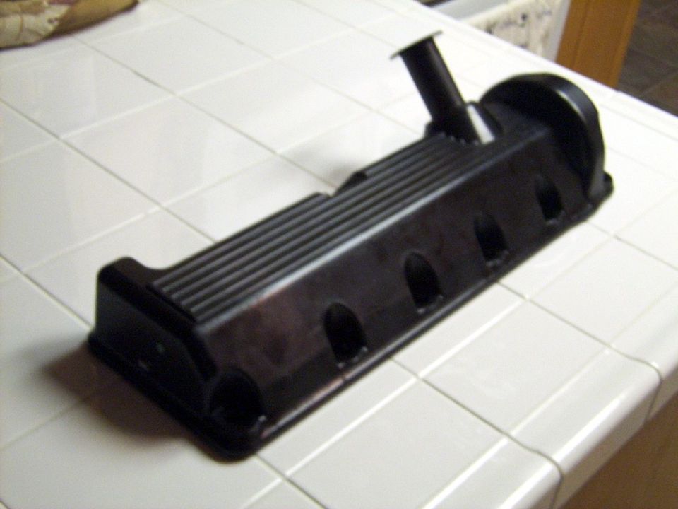 Black ribbed valve cover with breather tube resting on white tile countertop