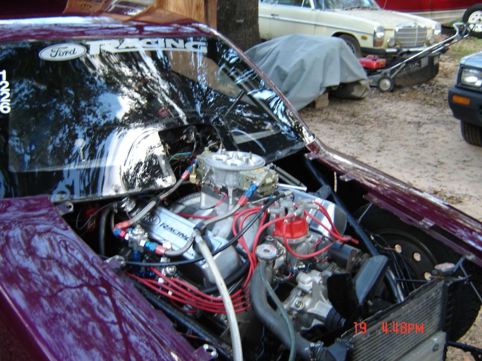 V8 engine with dual carbs and red plug wires in maroon car's engine bay, Ford Racing hood