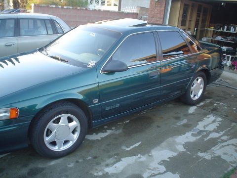 1993 Ford Taurus - A green sedan with tinted windows and a sunroof is parked in a driveway next to another vehicle.