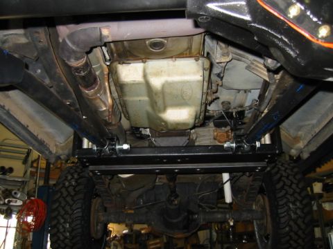 1992 Ford Bronco - Underside view of a vehicle on a lift showing a large fuel tank, exhaust piping, and a newly installed black steel crossmember/skid support…
