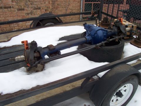 1994 Ford Bronco - A blue front axle assembly rests on a snow-covered trailer, with orange brake calipers visible.