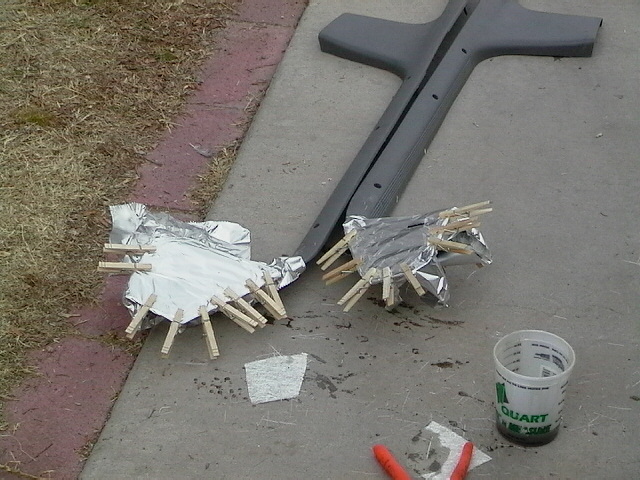 Two car parts wrapped in foil and secured with clothespins sit on concrete next to a gray trim piece