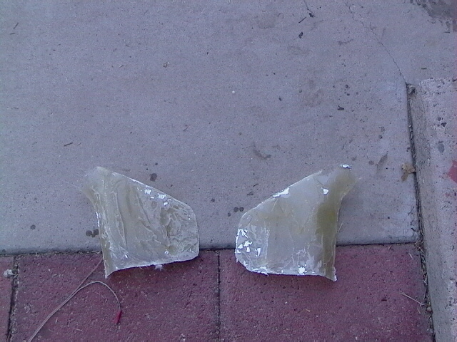 Two unfinished fiberglass automotive parts on a paved surface