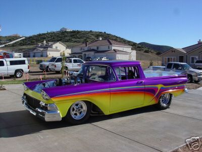 1973 Ford Ranchero - A custom pickup truck with a vibrant paint job and exposed engine sits in a driveway with other vehicles and houses in the background.