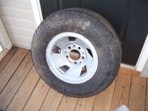 1988 Ford Bronco - A spare tire and rim rests on a wooden deck, with siding and a dark door in the background.