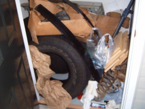 1988 Ford Bronco - A collection of automotive parts, including a tire, springs, and trim, are stored together.