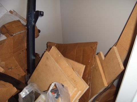1988 Ford Bronco - A black vehicle frame part with a mounting bracket is visible amongst cardboard boxes and other stored items.