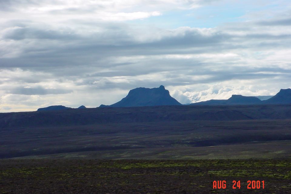 Dark volcanic plain and flat-topped mountain under cloudy sky, dated Aug 24 2001