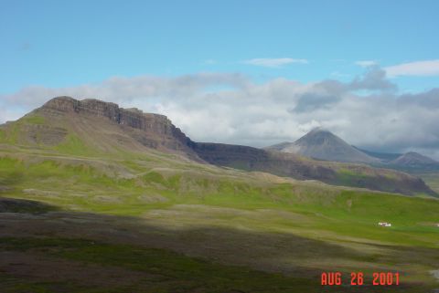 1993 Ford Bronco - A wide shot of a mountainous, grassy terrain with scattered clouds and a few distant structures.