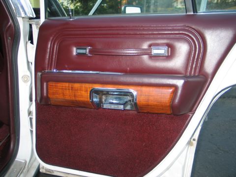 1988 Mercury Grand Marquis - Close-up of a car's interior door panel maroon upholstery, wood grain trim, and chrome accents.