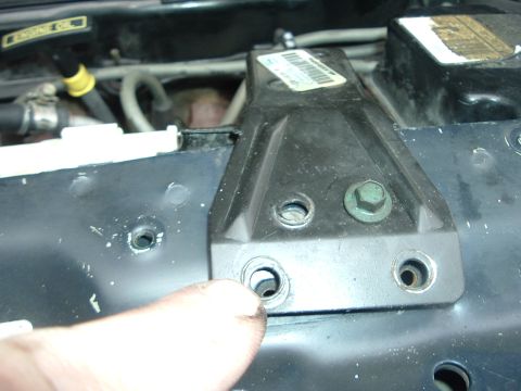 1993 Ford Taurus - A finger points to a hole in a black plastic bracket in a vehicle's engine bay.