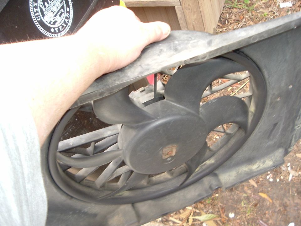 hand holding a black plastic radiator fan shroud with a fan visible inside