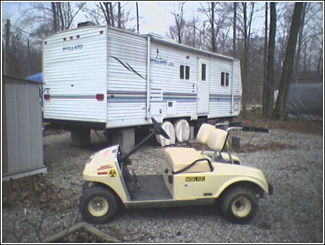 1993 Ford Bronco - A golf cart and a travel trailer are parked on a gravel lot next to a small shed.